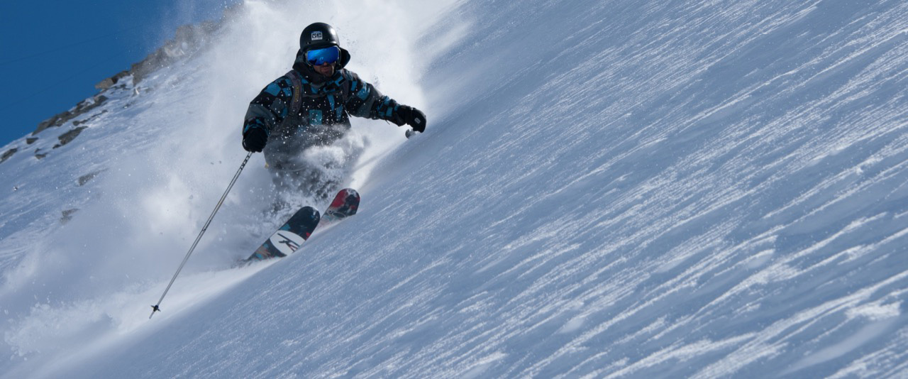 Skilehrer beim Skifahren abseits der Piste mit blauem Himmel im Hintergrund