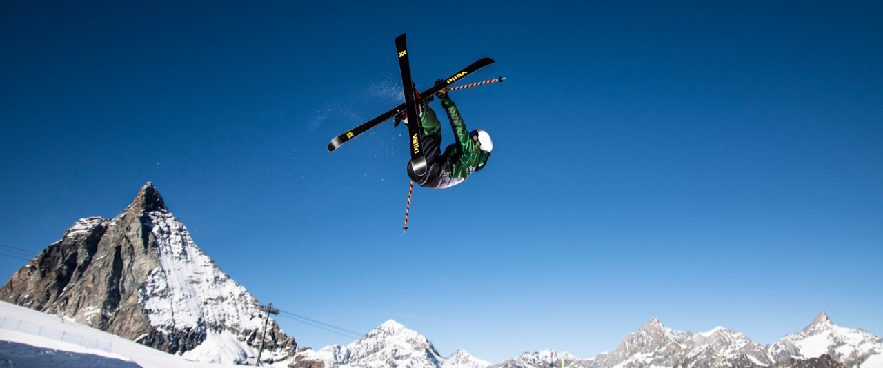 Instructor de esquí realizando un truco llamado flatspin 540 mute con el Matterhorn de fondo