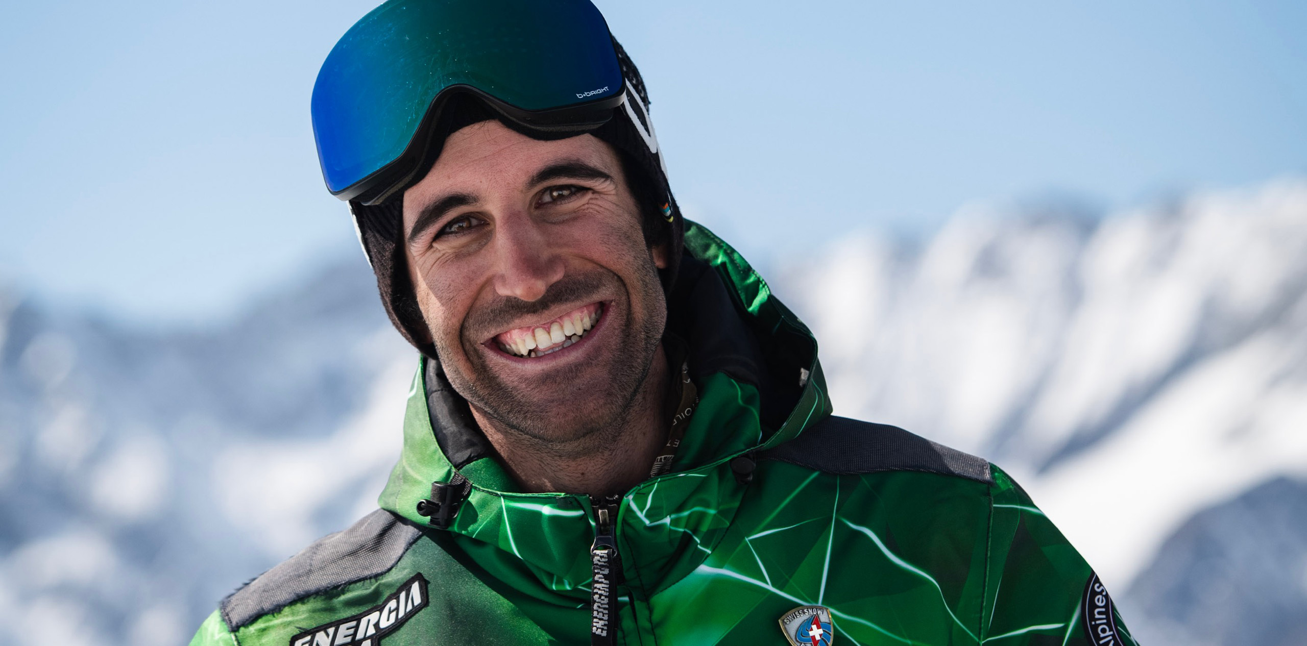 Instructor de esquí con uniforme, sonriendo, con las manos en las caderas, las montañas de Zermatt en el fondo