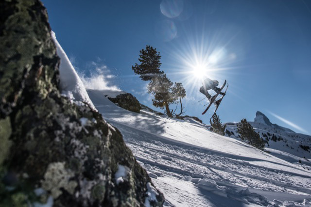 Instructor de esquí saltando desde un acantilado agarrando los esquís en un día soleado con el Matterhorn de fondo