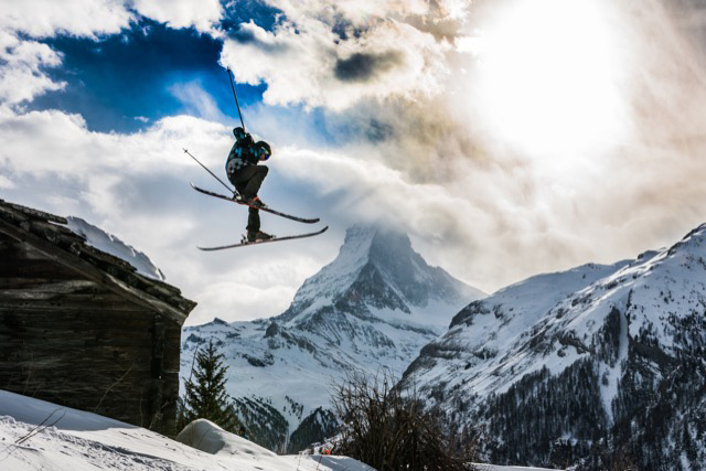 Skilehrer springt von einem Felsen mit dem Matterhorn im Hintergrund, das von einer Wolke verdeckt wird