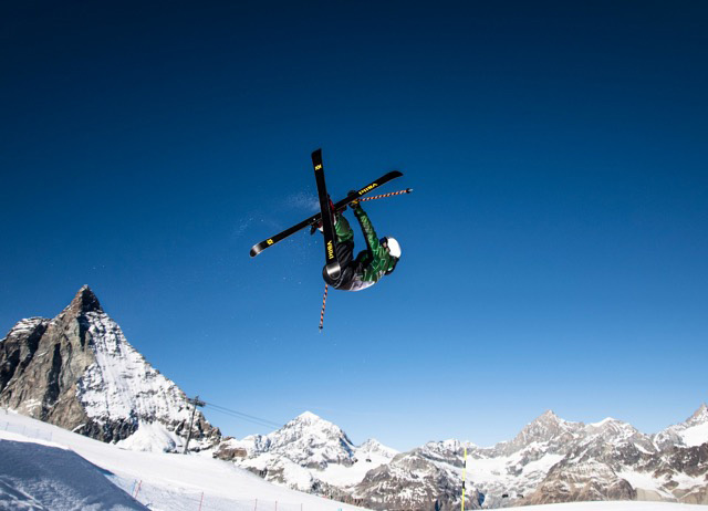 Instructor de esquí realizando un truco llamado flatspin 540 mute con el Matterhorn de fondo